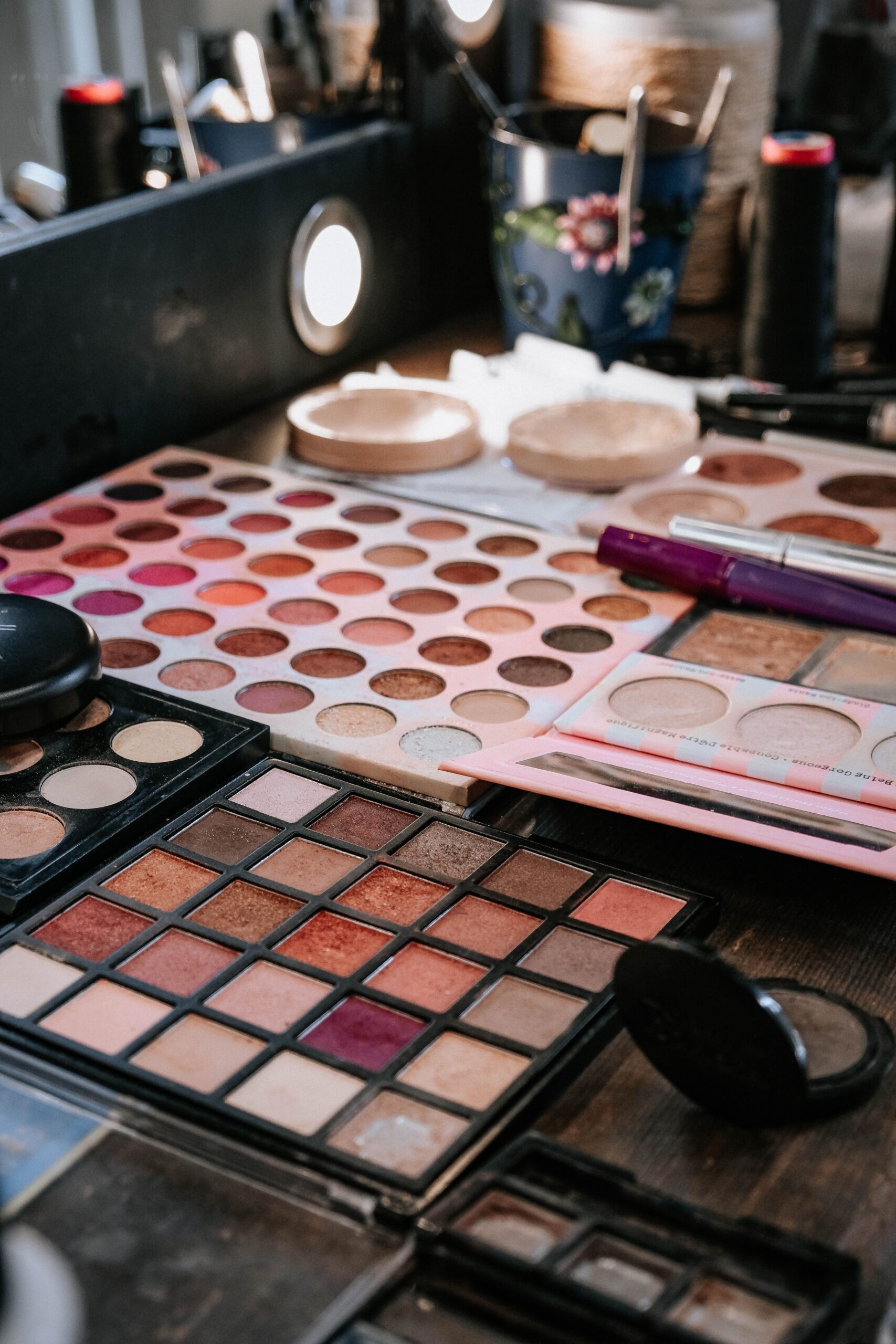 Assorted makeup palettes and cosmetics arranged on a vanity table.